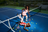 A model in a pink dress and white socks leans on a tennis net, another in red and white lies on the blue court.