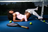A person in pink shorts lies on a blue court, with a tennis net behind them. A tennis racket is at the bottom.