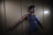 A person in a blue shirt with an arm extended against a light brown wall, partially visible in dim lighting.