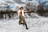 A model wears sunglasses, a black bra, white fur vest, olive cargo pants, and black boots in a snowy landscape.