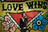 A model in a black suit jacket, white shirt, and glasses talks on a phone against a yellow and red graffiti wall.