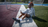A person in a patterned grey top and white socks lies on artificial turf, holding a phone, on a sunny day.